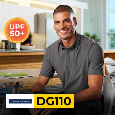 Smiling man wearing Devon & Jones DG110 CrownLux Performance polo shirt with UPF 50+ in a modern indoor setting