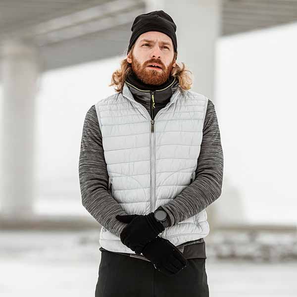 man wearing grey puffer vest layered winter outdoor apparel with gloves and beanie